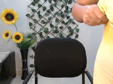 Video of a person in yellow clothing facing a black chair with a floral wall backdrop featuring sunflowers and green leaves.