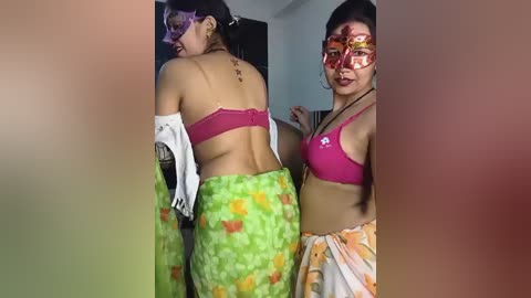 Video of two South Asian women, one with a red bindi, wearing vibrant traditional clothing, standing side by side in a brightly lit room.