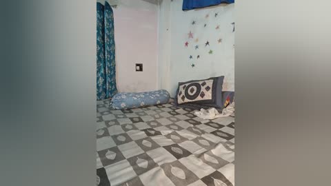 Video of a small, simple bedroom with a bed covered in a gray and white patterned blanket, a blue and white pillow, and a stuffed octopus toy on the floor.