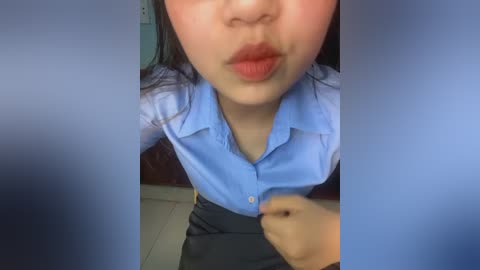 Media: A video shows an Asian woman with light skin, straight black hair, and red lipstick, wearing a light blue button-down shirt and black skirt, puckering her lips. The background is blurred.