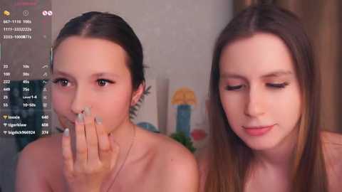 Media: Video of two young women in a cozy room; one with dark hair and the other with brown hair, both with light skin. They're looking at a phone displaying a calendar.