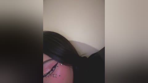 Video of a person with long black hair, wearing glasses, lying face down with a visible bruise on the cheek, against a blurred beige background.