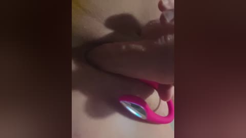 A dimly lit, close-up video shows a person with fair skin using a pink and blue vibrator on their chest, casting a shadow.
