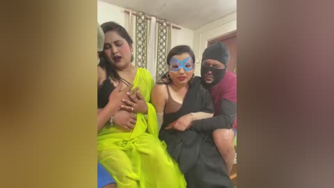 Video of three people: a woman in neon green, a woman in black, and a masked man, sitting in a domestic setting with curtains and a wooden door in the background.