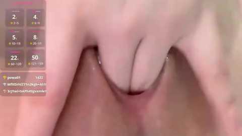 A close-up video shows a Caucasian woman's hand with a ring and a pinky finger on her left breast, partially obscured by her other hand. The background is blurred, with a digital overlay showing a game screen.