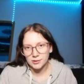 Media: A video of a young woman with fair skin, long brown hair, and glasses, wearing a grey hoodie, standing in a dimly lit room with blue LED strip lights on the wall.