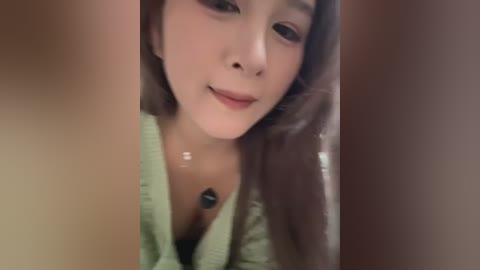 A close-up video of an Asian woman with fair skin, brown hair, and a light green blouse, taken from a low angle.