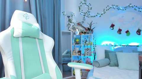 Video of a modern, pastel-colored gaming room with a white and mint green gaming chair, a blue gaming desk, and a white bookshelf adorned with holiday stockings.