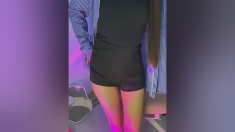 Video of a woman's lower body in black shorts, standing in a dimly lit room with purple lighting, wearing a blue-striped shirt, and a white sneaker nearby.