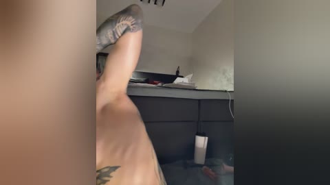 Video of a woman in a dimly-lit room, mid-throw, wearing black socks and a tattoo on her left arm, standing on a carpeted floor with a white cup beside her.