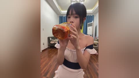Video of an Asian woman in a maid outfit, eating a bread sandwich, in a modern, brightly lit room with wooden floors and blue curtains.