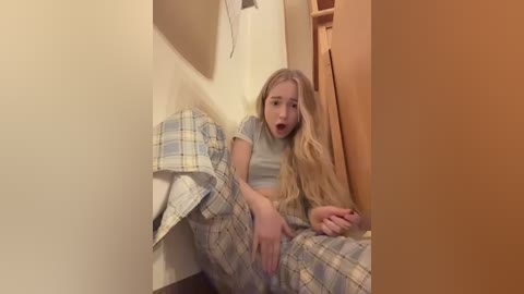 A video of a blonde woman in a plaid nightgown, lying on a bed, mouth open in surprise.