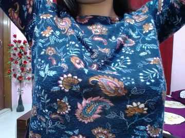 A video of a person wearing a dark blue paisley-patterned shirt with floral designs, standing indoors with a red wall and a purple table in the background.