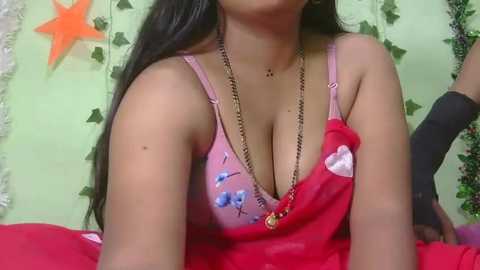 Media: A video of a young woman with medium skin tone and long black hair, wearing a pink bra with blue floral embroidery and a red saree.