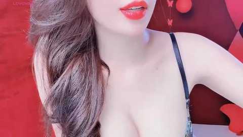A video of a young Asian woman with long, wavy brown hair, wearing a black lace bra, against a red background with heart-shaped confetti.