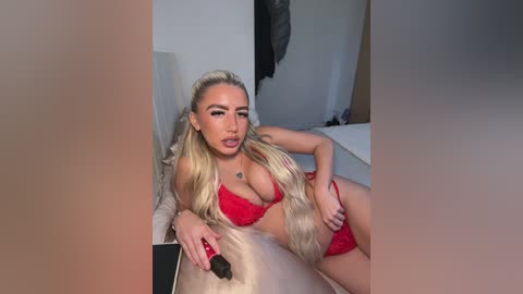 Video of a blonde woman with long hair, wearing red lingerie, lying on a bed in a dimly lit bedroom, holding a makeup brush.