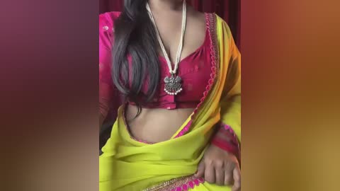 Media: Video of a South Asian woman in a vibrant pink blouse, yellow sari, and gold necklace, against a gradient background of red, orange, and yellow.