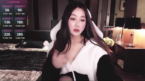Media: A video of an East Asian woman with long black hair, wearing a white and black nun outfit, in a dimly-lit bedroom with a bed, nightstand, and lamp.