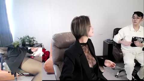 Video of an office scene with a woman in a black suit and a man in a white shirt. Another woman in a black dress is in the background.