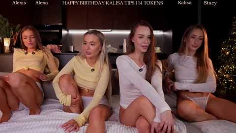Video of four young women in lingerie, sitting on a bed in a dimly lit room with Christmas decorations.