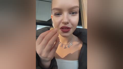 A video of a young woman with pale skin, dark hair, and red lipstick, wearing a black jacket over a white top, eating a cookie, with blurred faces in the foreground.