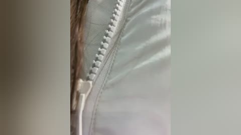 A close-up video of a partially unzipped, light blue jacket with a white zipper and textured fabric, showing the inner lining. The background is a plain, light gray wall.