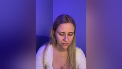 Video of a young Caucasian woman with long blonde hair, fair skin, and a nose ring, wearing a white top, standing against a blue and purple gradient background.