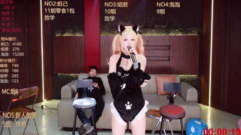 Video of an Asian woman in a black catgirl outfit, holding a microphone, surrounded by a live broadcast setup with two men.