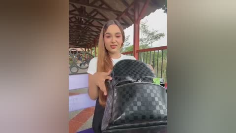 Video of a young Asian woman with long, straight hair, wearing a white t-shirt, pushing a black designer stroller with a checkered pattern on a wooden deck.