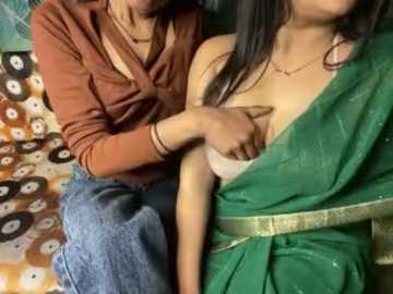 Video of a woman with long black hair, wearing a green sari and a gold belt, being breastfed by a woman in a rust-colored top.