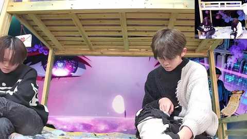 Video of two young boys in a bed with a colorful, dreamy backdrop featuring a large eye, purple hues, and a floating figure. The boys wear dark, textured clothing.