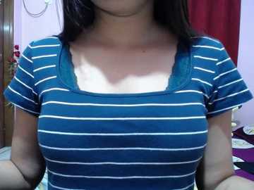 A video of a woman wearing a blue and white striped top, with her face partially cropped out, in a room with purple walls, a red curtain, and a wooden door.