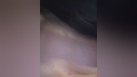 A close-up video of human skin with a smudged, indistinct appearance. The background is dark, with a blurred, abstract texture. The image lacks distinct features, making it difficult to discern details or context.