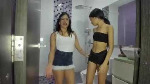 Video of two Asian women in a modern bathroom; one in a white top, denim shorts, and headband, the other in a black bandeau and shorts.
