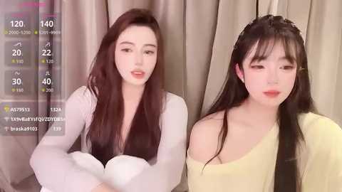 Media: A video featuring two East Asian women with fair skin, long dark hair, and red lipstick, wearing off-shoulder tops, one in white, the other in yellow.