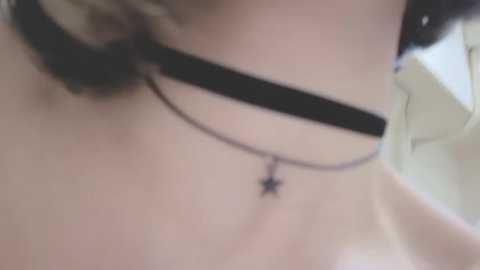 A close-up video of a person's neck, wearing two black chokers with a small star pendant between them. The skin is light-toned and the background is blurred.