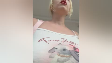 Video of a fair-skinned woman with blonde hair, wearing a white tank top with a pink bow and \"Faux Fur Rabbit\" logo, seen from a low angle.
