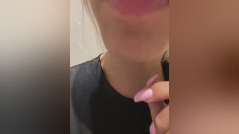 A close-up video of a woman with fair skin and blonde hair, wearing a black shirt. Her lips are painted a bold pink.