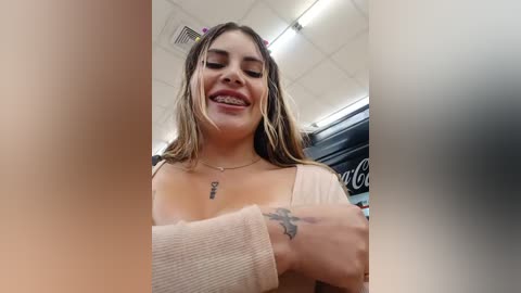 Video of a young woman with light skin, long brown hair, braces, and a tattoo on her forearm, smiling in a brightly lit store.