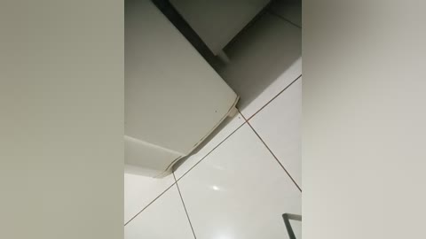 Video of a ceiling in a modern, minimalist bathroom showing a rectangular, white exhaust fan mounted flush against the white, glossy tile wall. The fan is positioned near the top center of the image, with clean, straight lines and a smooth, uncluttered aesthetic.