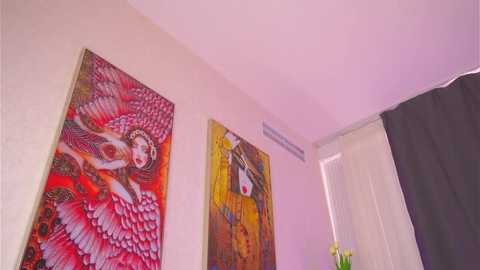 Video of a modern, minimalist room with two vibrant, abstract paintings on light beige walls; one features a stylized angel with red wings and the other a surreal, masked figure.