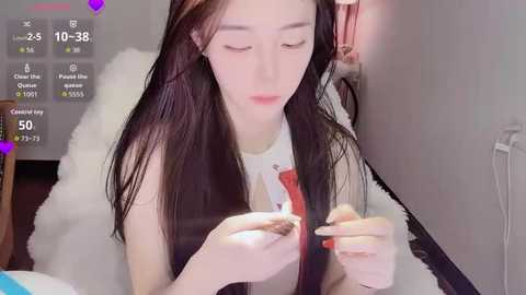 Video of a young East Asian woman with long black hair, wearing a white shirt, braiding her hair in a cozy room with a white rug and a wooden chair.