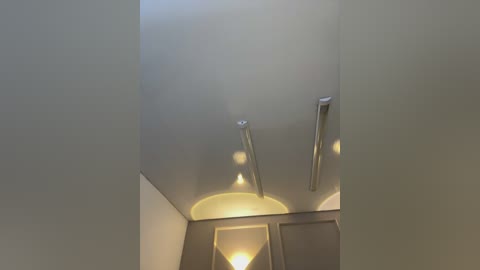 Video of a minimalist, modern interior ceiling featuring sleek, silver ceiling lights and a soft, ambient yellow light from a wall-mounted fixture. The walls are painted in a light, neutral color, creating a clean, contemporary atmosphere.