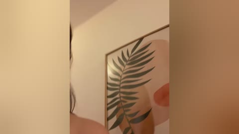 Video of a beige wall with a large framed fern print. The image is slightly blurry and out of focus, with no visible people or objects in the foreground.