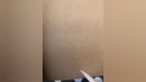 A close-up video of a light-skinned person's upper arm, showing fine hairs and a smooth texture. A black-and-white checkered pattern is visible at the bottom, possibly indicating clothing. The image is blurry, making details unclear.