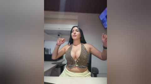 Video of a curvy Latina woman with long black hair, wearing a low-cut, sequined brown top and white pants, standing with fists raised in a modern office.