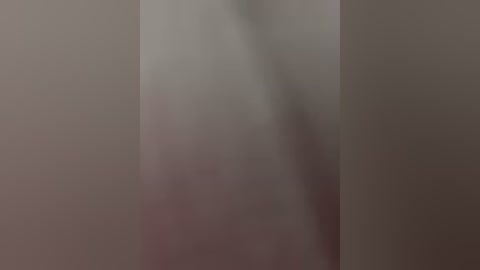 A blurry video of a person's back, partially obscured by a light-colored, textured wall. The individual's shape is indistinct, with a soft, out-of-focus quality, suggesting a close-up view.