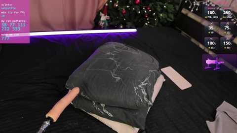 A video of a person lying on a bed with a black sheet, holding a gray pillow with a carved wolf design. The background includes a Christmas tree and digital gaming overlays, suggesting a gaming environment.