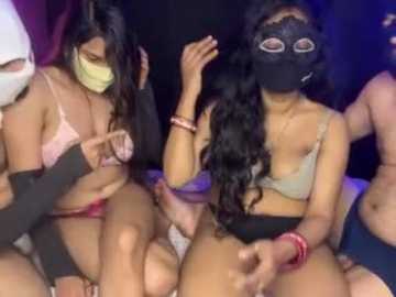 Media: Video of two women in a dimly lit room, one wearing a mask, holding a large dildo, both topless in lingerie, surrounded by others.