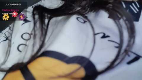 A close-up video of a person wearing a black-and-white striped shirt with a yellow collar, lying face down on a bed. The image is overlaid with a \"Lovense\" watermark and a chat text.